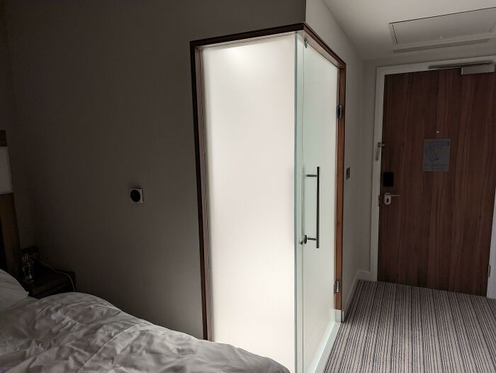 Small bathroom with frosted glass door inside a hotel room showing a dumb interior design decision.