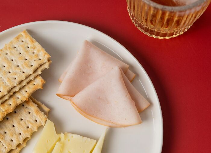 Turkey slices, cheese, and crackers on a white plate with a drink, illustrating common foods that spoil quickly.