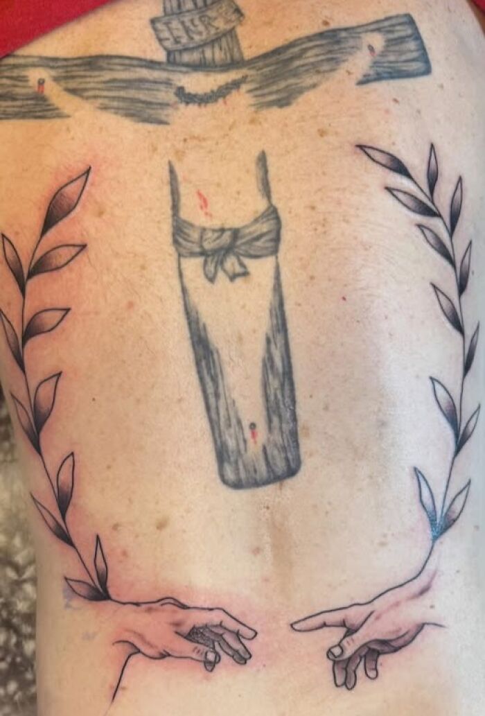 Tattoo of a crucifix with hands and leaves on a person's back, showing an inked design with visible imperfections.