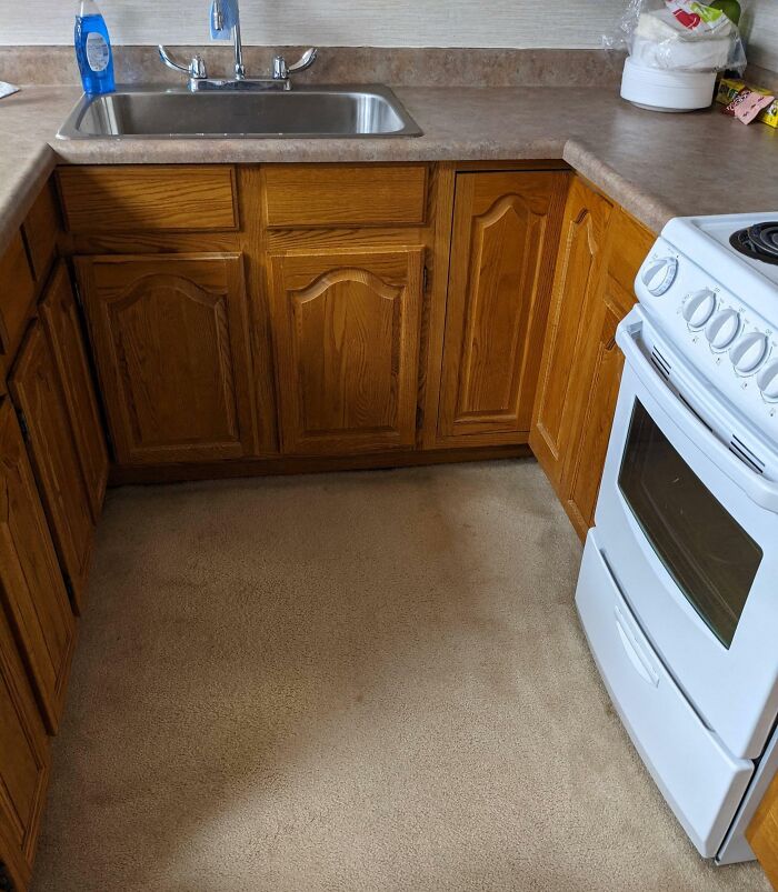 Kitchen with carpeted floor, wooden cabinets, and white stove showing dumb interior design decisions.