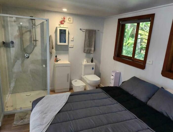 Small bedroom with a bed, shower, toilet, and sink all combined, showcasing dumb interior design decisions.