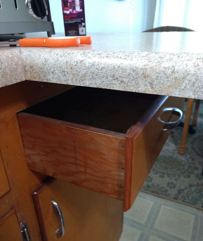 Partially opened wooden kitchen drawer blocked by a thick countertop edge showing poor interior design decision.