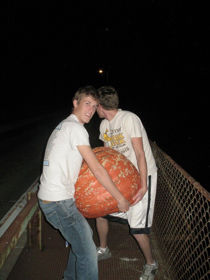 Two young men carrying a large pumpkin at night, sharing a moment in a found photos collection.