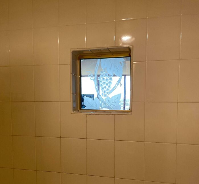 Small square window with decorative grapevine design surrounded by beige tiles illustrating dumb interior design decisions.