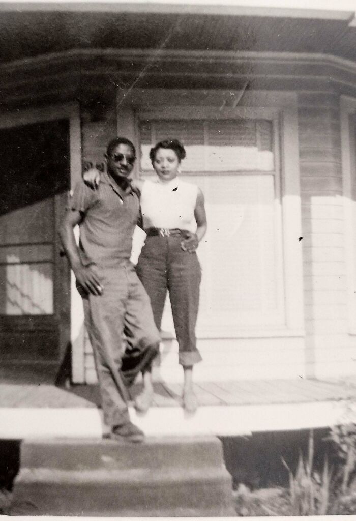Man and woman posing together on a porch in a vintage found photo shared by people in casual clothing.