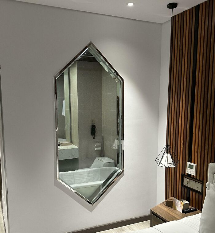 Bathroom visible through an unusual interior design mirror cut into bedroom wall, showing dumb interior design decisions.