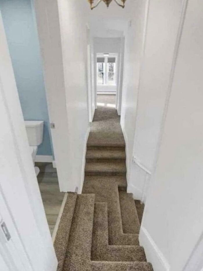 Narrow hallway with a confusing multi-level carpeted staircase showing dumb interior design decisions.