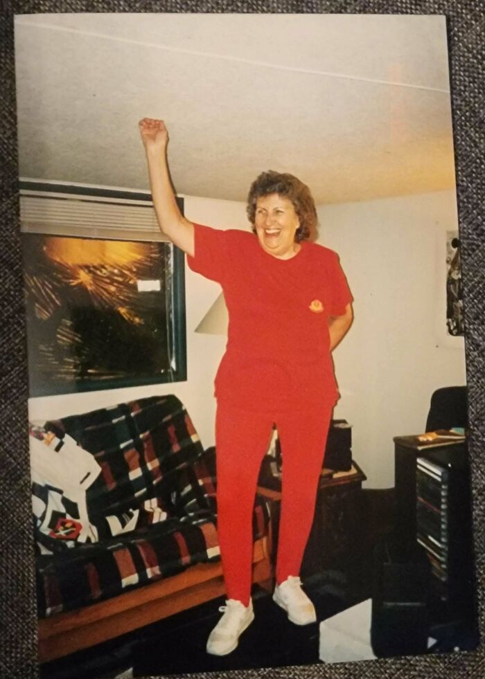 Woman in red outfit smiling and raising arm inside a cozy living room, sharing found photos moment.