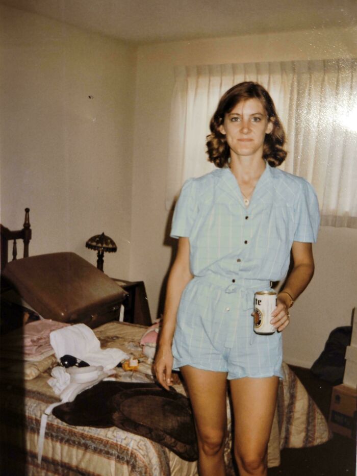 Woman in vintage outfit holding a can in a bedroom with unpacked luggage, a found photo shared by people.