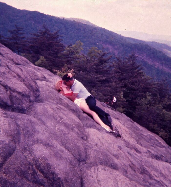 Couple sharing a romantic moment on a rocky mountain slope surrounded by trees and scenic views, people share found photos.