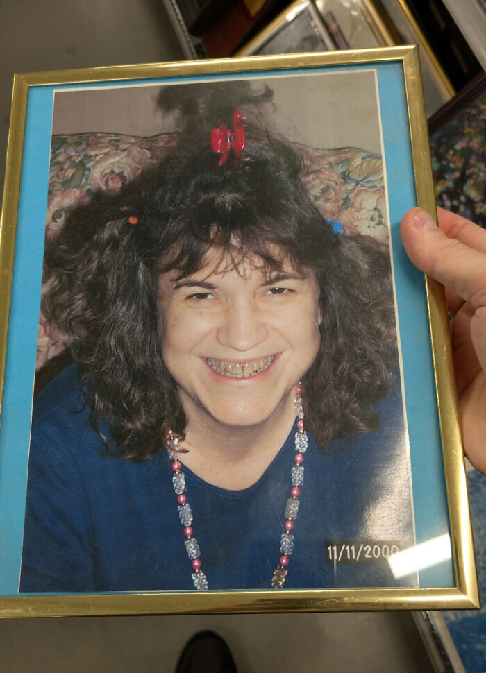 Person holding a framed found photo of a smiling woman with curly hair and colorful hair clips, sharing a found photo moment.