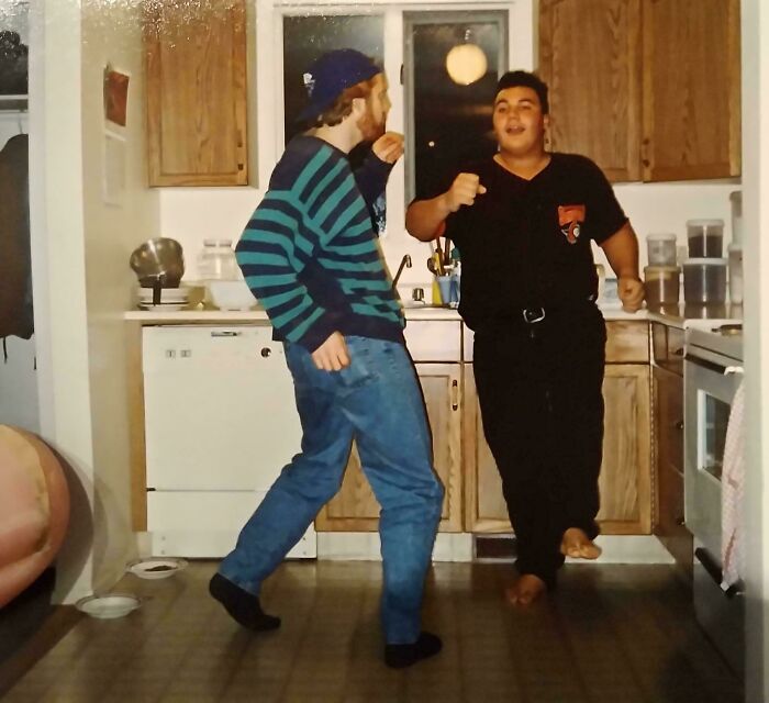Two people share found photos while dancing and having fun together in a cozy kitchen setting.