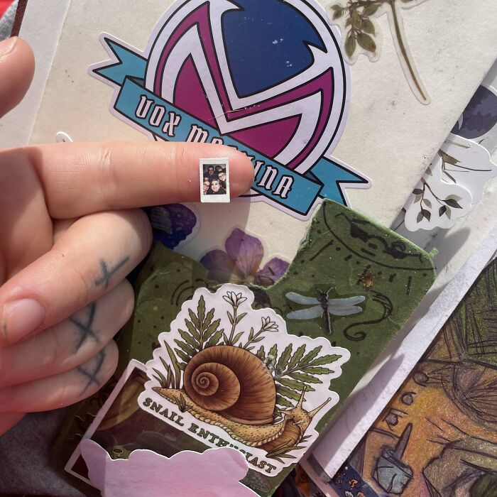 Person holding a tiny found photo pinched between fingers amid stickers and art in a creative collage scene.