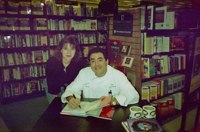 Man signing book at a table with woman nearby in a bookstore, people share found photos capturing the moment.