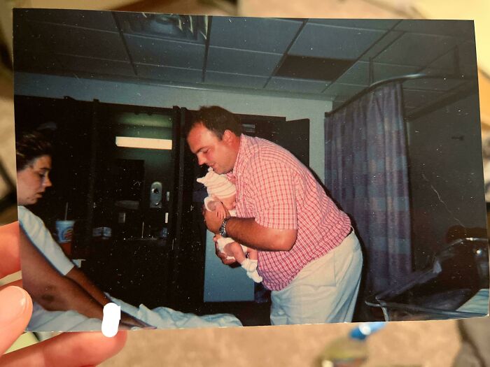 Person in a hospital room holding a newborn baby while another person watches, a moment from people share found photos.
