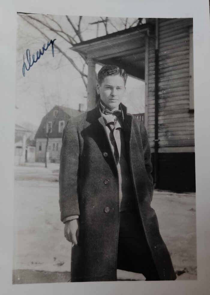 Young man in vintage coat standing outside a house in winter, a found photo shared by people.