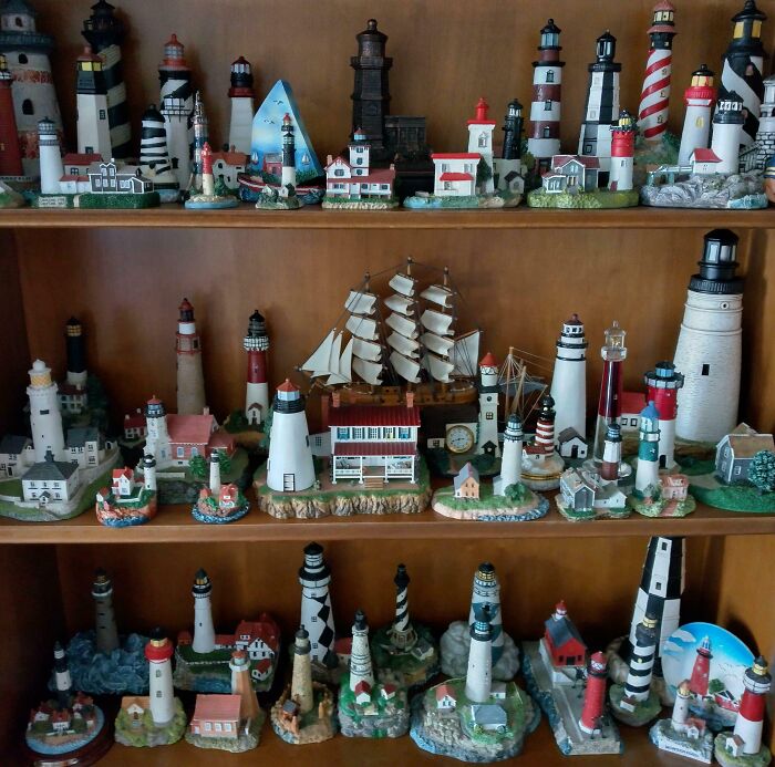 Collection of unusual lighthouse miniatures and model ships displayed on wooden shelves in a home setting.