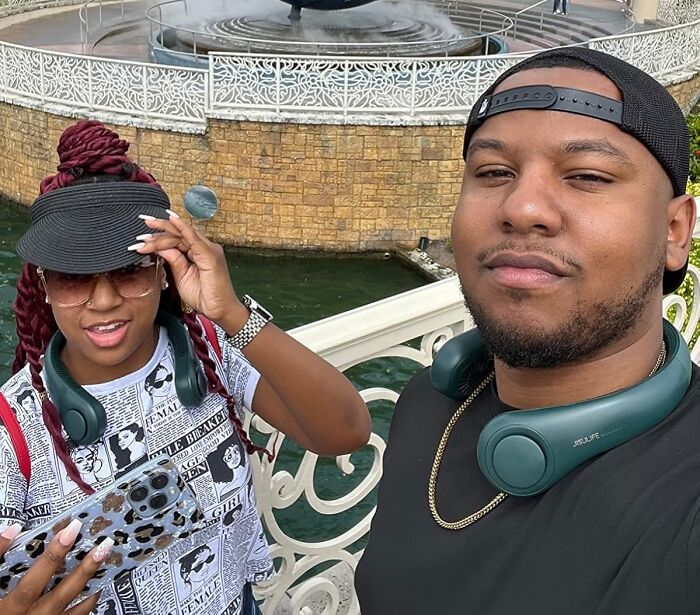 Two people wearing wireless neckband headphones outdoors near a decorative fountain, popular Amazon movers and shakers product.
