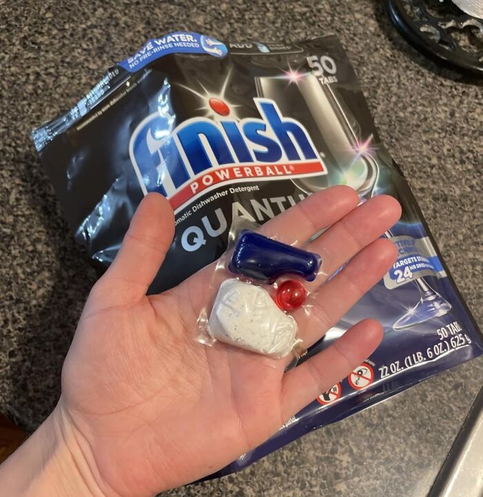 Hand holding an Amazon movers and shakers dishwasher detergent pod in front of a Finish Powerball package.