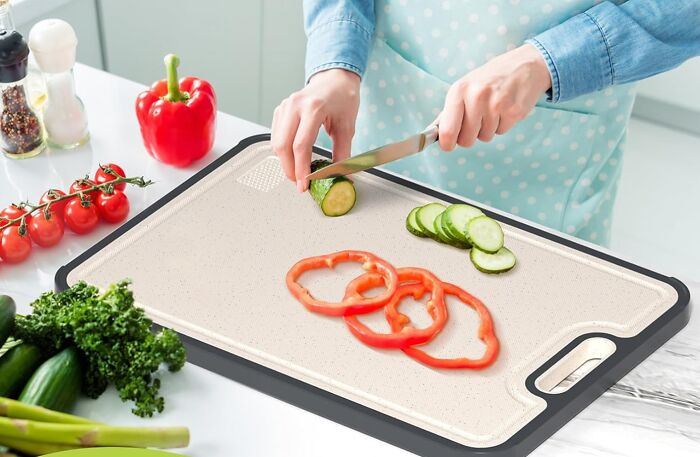 Person slicing cucumber on a cutting board with red bell pepper and fresh vegetables, popular Amazon movers and shakers product.