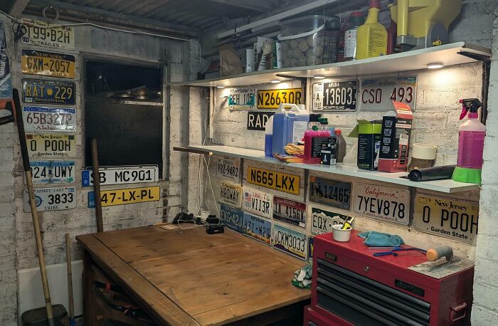 Collection of unusual and interesting license plates displayed on walls in a home workshop or basement setting