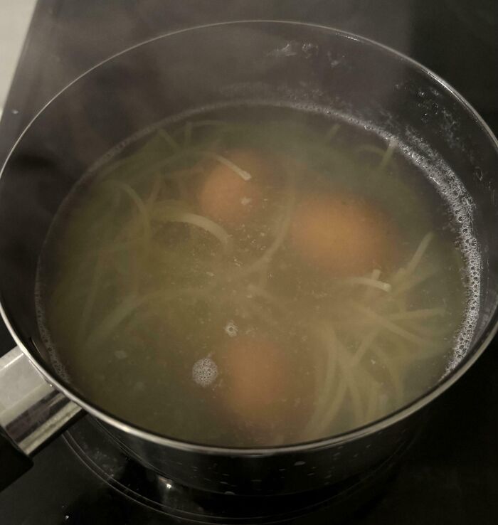 Pot boiling with spaghetti and whole eggs inside, illustrating a cooking fail and accident in the kitchen.