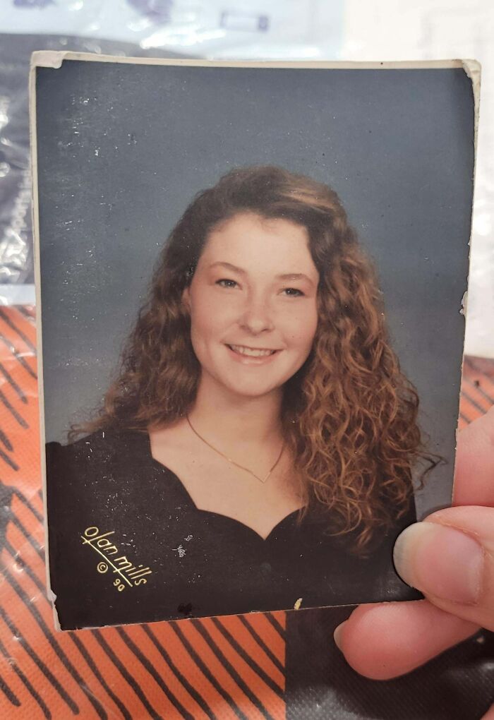 Hand holding found photo of young woman with curly hair smiling in a vintage portrait, people share found photos.