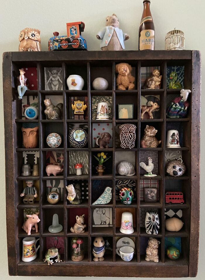 Wooden display case with an unusual collection of small figurines, toys, and curiosities in a home setting.