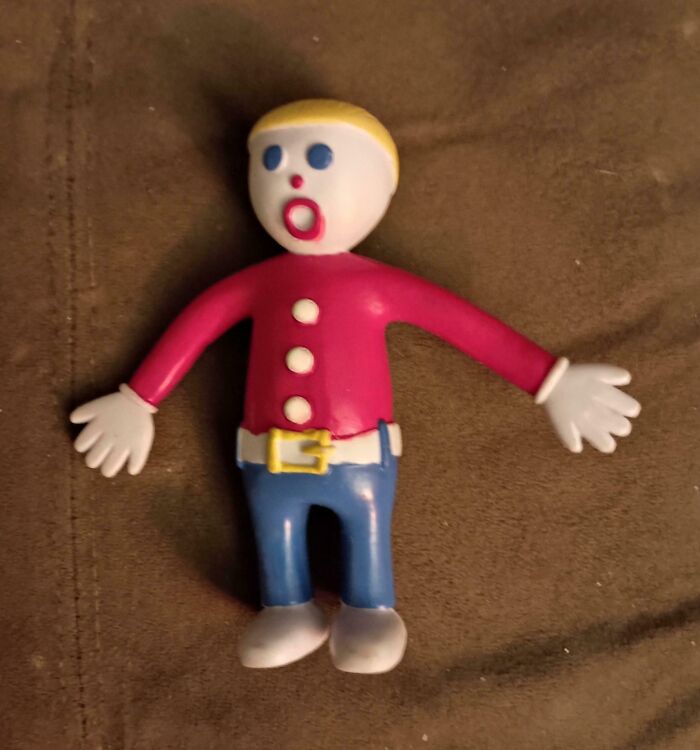 Nostalgic plastic toy figure with blonde hair, red shirt, blue pants, and white gloves on a brown fabric background