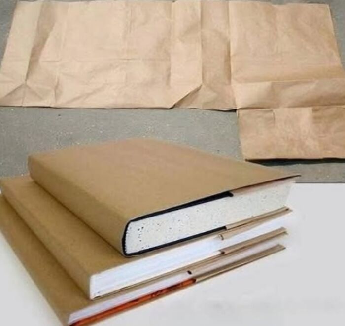 Three books wrapped in brown paper with extra paper laid out, evoking nostalgic memories of school days.