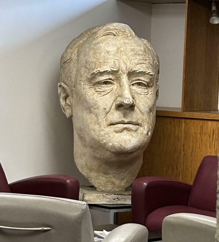 Large stone bust of a man displayed in a corner chair setting, illustrating fascinating pictures for curious minds.
