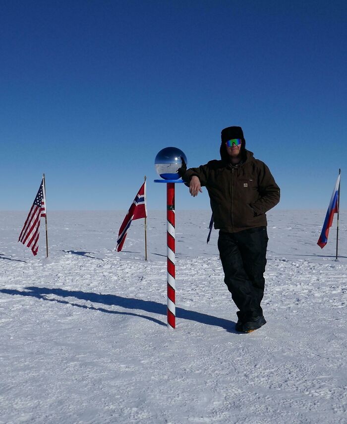 Person in winter clothing leaning on a pole with flags on snow-covered ground, fascinating pictures for curious minds.