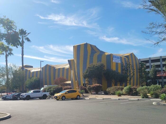 Striped building shaped like a giant shoe with parked cars nearby, an intriguing picture for curious minds to learn more.