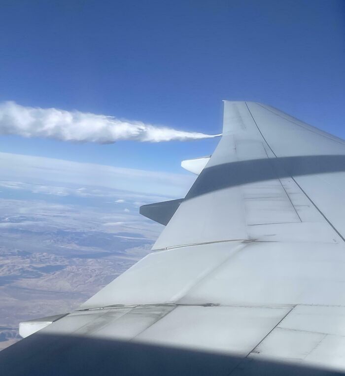 View from airplane window showing wing with clear sky and landscape below, perfect for curious minds who want to learn more.