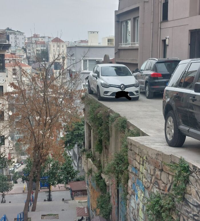 Cars parked precariously on a narrow ledge above city street, showcasing a fascinating picture for curious minds.
