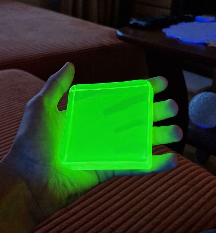 Hand holding a glowing green square object emitting light in a dark indoor setting for curious minds to learn more.