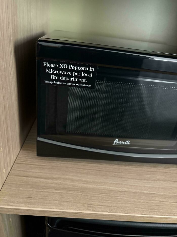 Microwave in hotel room with a sign warning no popcorn allowed per local fire department for safety.