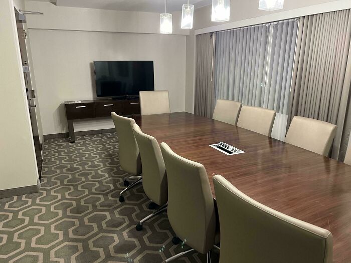 Modern hotel meeting room with large wooden table, beige chairs, TV, and geometric carpet design reflecting creative hotel design decisions.