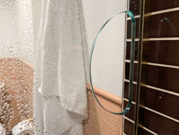 Fogged glass shower door with water droplets and a round magnifying mirror, showcasing creative hotel design decisions.