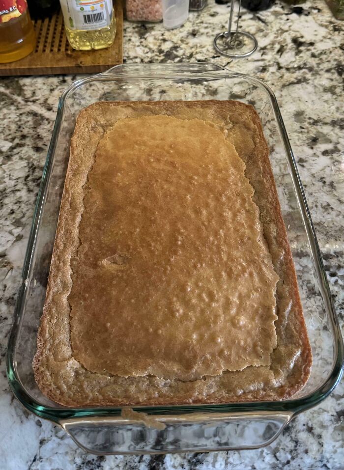Baked dish with uneven surface and c*****d edges in a glass pan on a kitchen countertop cooking fail