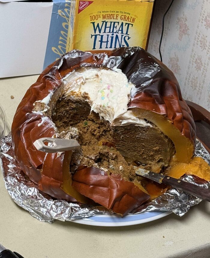 Burnt and collapsed pumpkin cake with frosting, showing a hilarious cooking fail and accident on a kitchen counter.