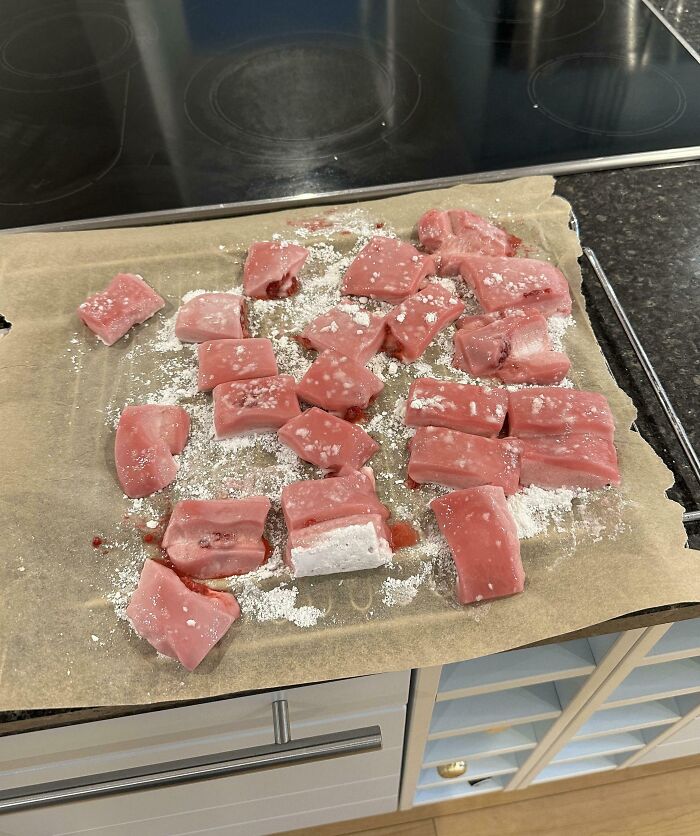 Raw pink dough pieces covered in flour on parchment paper, showcasing a funny cooking fail with food preparation gone wrong.