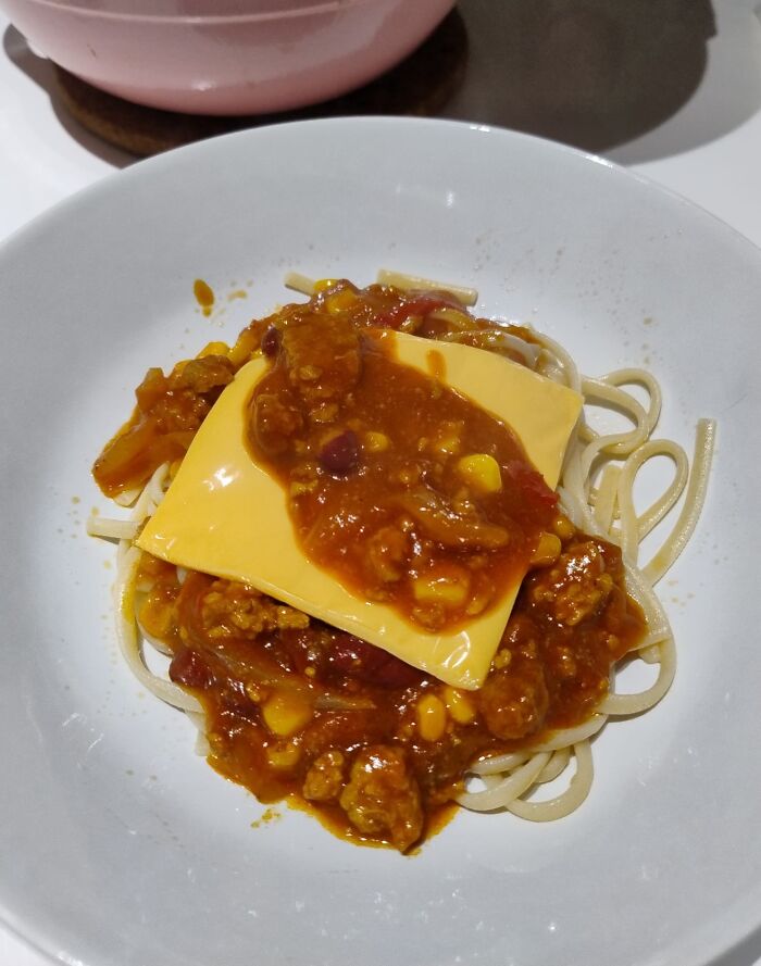 Spaghetti topped with a slice of processed cheese and chunky sauce, illustrating a cooking fail accident.