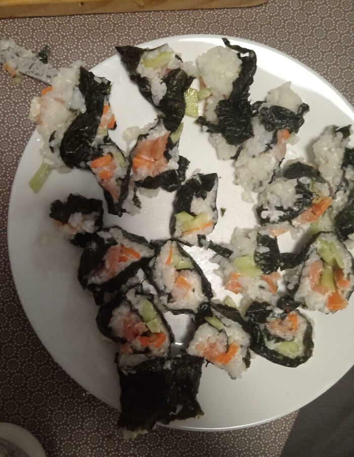 Poorly rolled sushi with rice falling apart on a white plate, showing a cooking fail and accident in the kitchen.