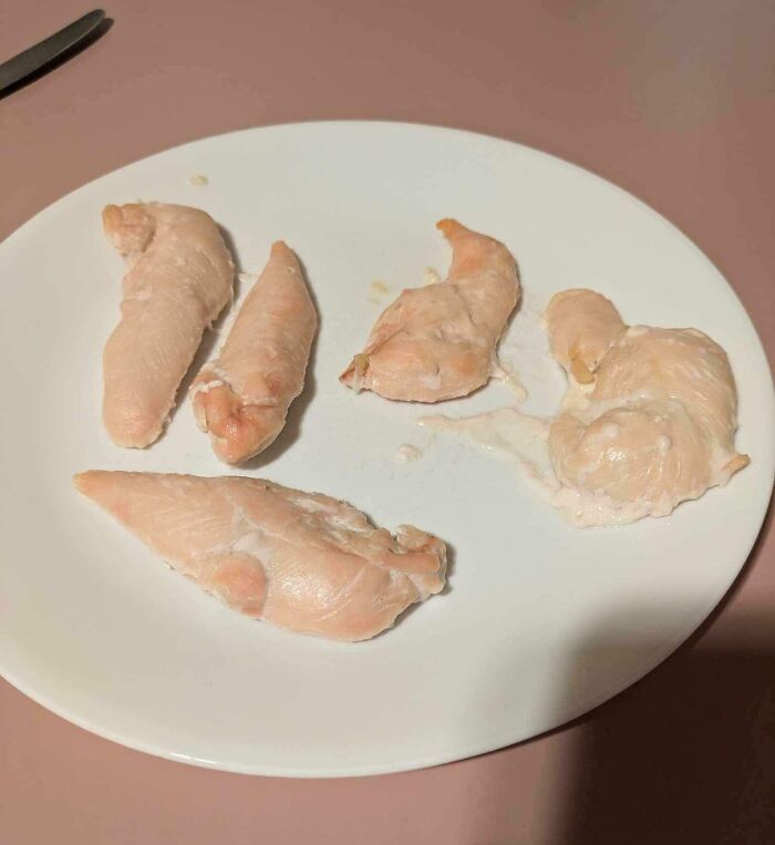 Partially cooked raw chicken pieces on a white plate showing a painful cooking fail in the kitchen.