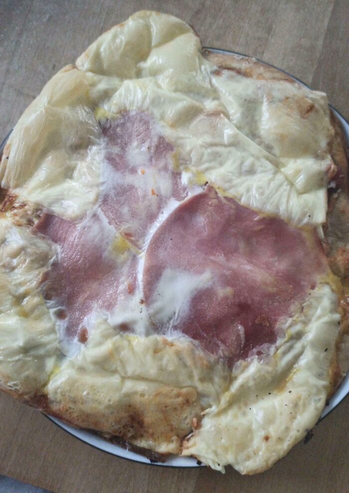 Poorly melted cheese and ham on a pizza showing a clear cooking fail and kitchen accident.