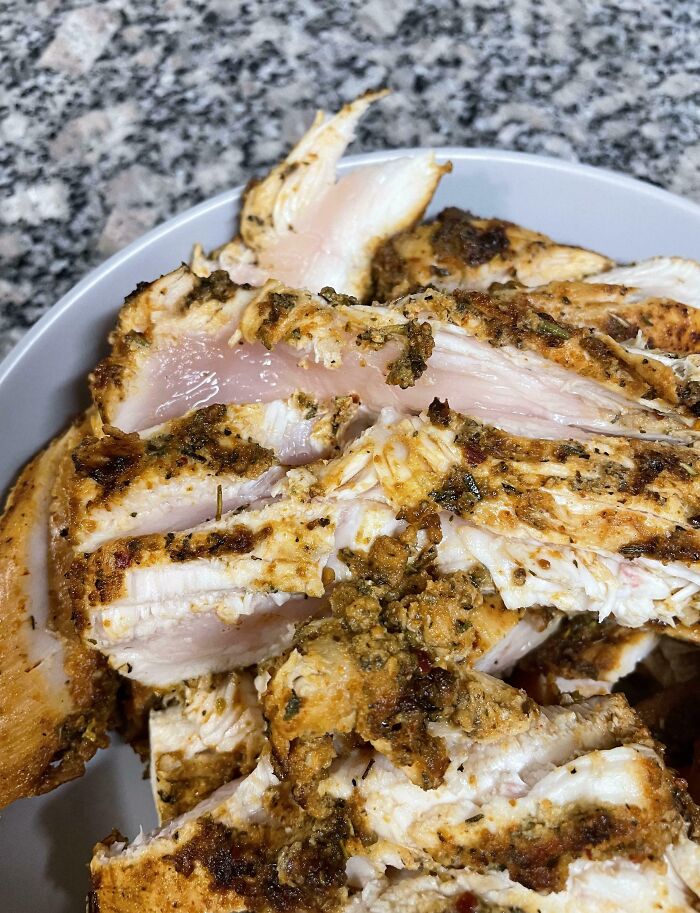 Undercooked chicken with pink, raw spots showing a dangerous cooking fail on a white plate against a granite countertop.