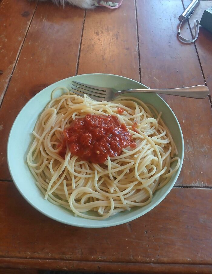Bowl of spaghetti with red sauce on a wooden table and a fork, illustrating a cooking fail moment.