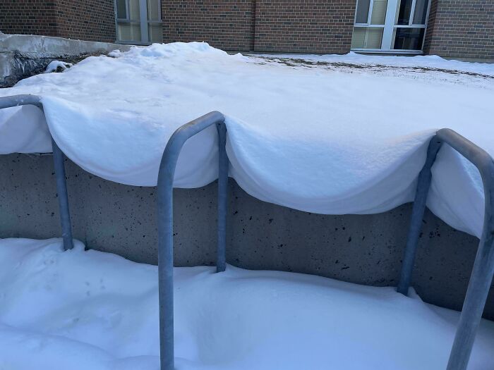Snow draped over a bike rack creates an interesting shape requiring a double take to realize what it really is.