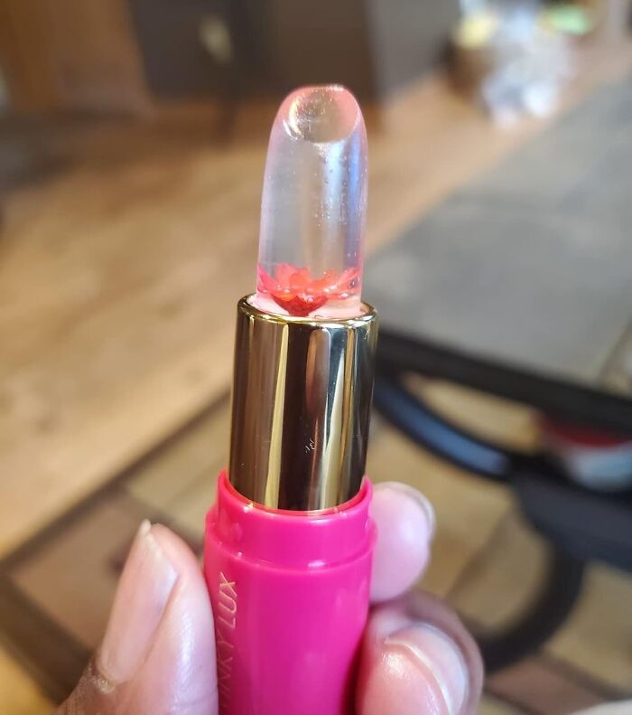 Clear lipstick with embedded red flower held in hand, an unexpected find for instant mood lift and happiness boost.